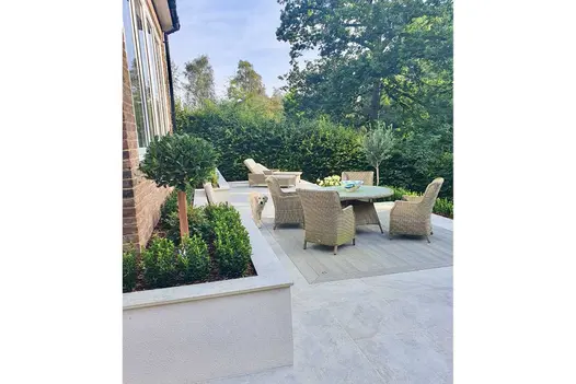 Luxury rattan furniture on Smoked Oak Enhanced Grain Millboard Decking set into Porcelain Paving on patio terrace with raised beds.