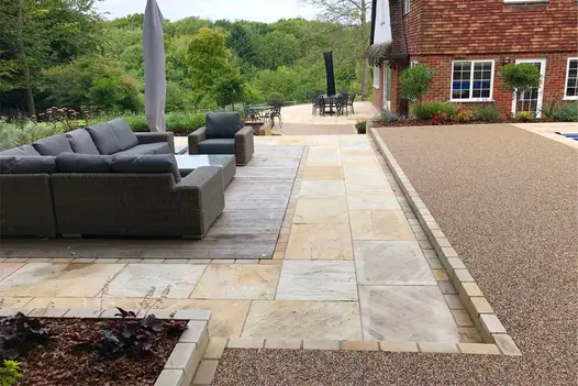 Tumbled Mint Sandstone Setts line paved area next to planted raised bed and fence and wall water feature cascading into pool.