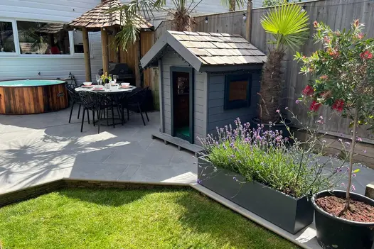 Hot tub, tiki bar and small shed sit on porcelain paving, flanked by bullnose steps leading to lawn area.