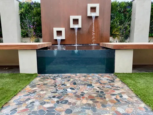 Two pillars clad with desert beige designclad porcelain cladding sit either side of corten water feature.