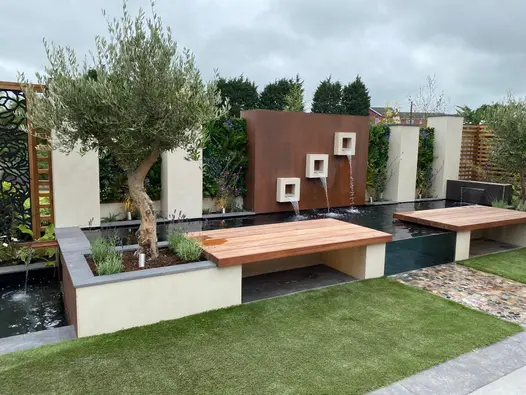 Olive trees sit either side of raised bedding water feature, using desert beige designclad porcelain cladding.