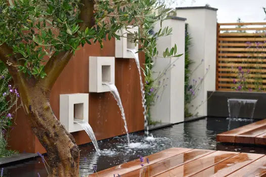 Close up through olive tree next to raised bedding water feature, using desert beige designclad porcelain cladding.