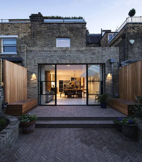 Rear of terrace property with large extension with picture window opening onto narrow garden paved with Westminster brick pavers.