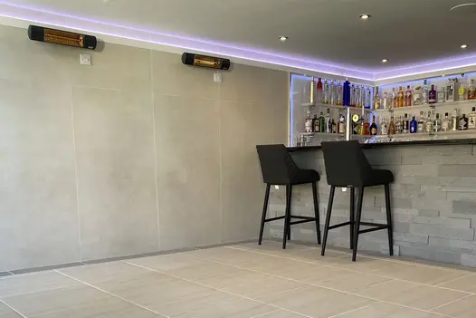 Two barstools sit at bar clad in stone, walls of bar with heaters using desert beige composite cladding.