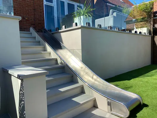 Metal slide leads down to lawn adjacent to steps, raised walls clad in desert beige designclad porcelain cladding.