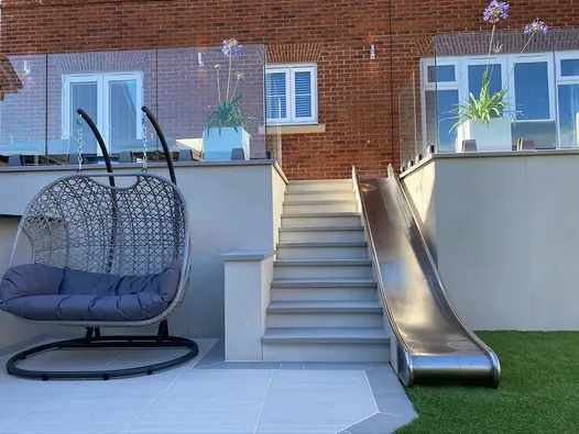 Metal slide next to set of stairs and egg chair, raised walls clad in desert beige designclad porcelain cladding.