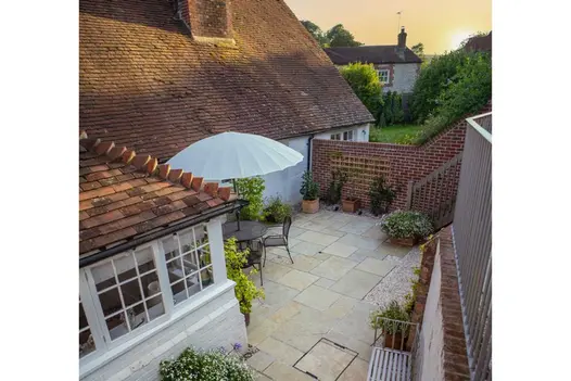Small courtyard of paved with patio pack of Antique Yellow limestone paving, with metal dining set and parasol next to cottage.