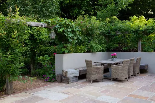 Raj Green Indian Sandstone patio with dining table leads off into a haven of greenery, through a wooden pergola.