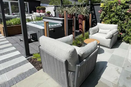Hot tub sits on grey Lucca brick paving laid stack bond, between 2 sets of furniture, next to striped path. Built by Olive Tree.