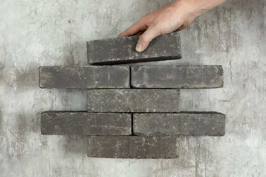 Hand puts single Lucca Clay Paver onto top of formation of 6 other bricks arranged in rows of 1 and 2. Free UK delivery available.