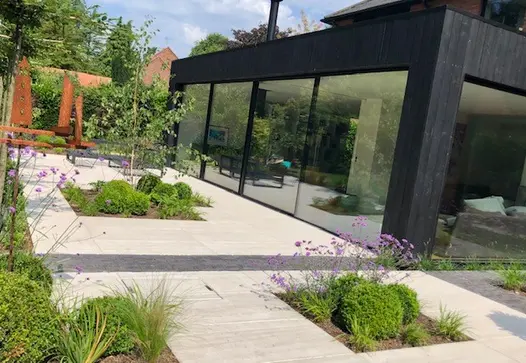 Modern glass-fronted extension faces onto paved patio interrupted by strips of Lucca clay bricks and rectilinear beds.