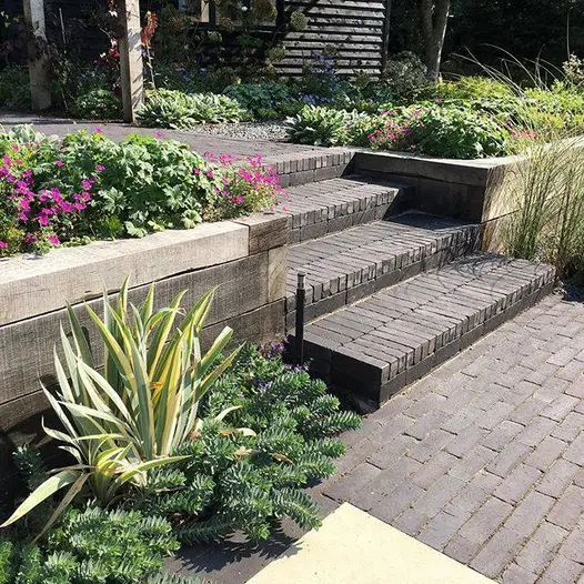 4 steps of Lucca clay pavers rise between retaining beds made of timber sleepers connecting 2 levels of garden paved in matching bricks