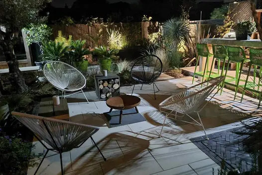 Garden paved with Lugano Dutch clay pavers and sawn sandstone, cluttered with seats, fire pit, log store, bar and potted palms.
