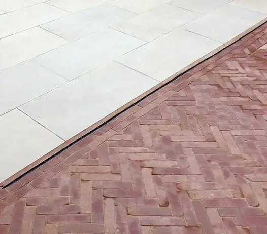 Cross section of light patio paving slabs and Roma clay pavers laid in herringbone style with a slot drain in-between.