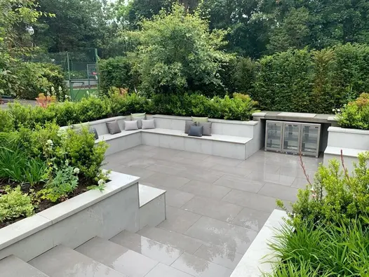 Large sunken garden seating area paved in Steel Grey porcelain with built in porcelain clad benches and raised planter beds.