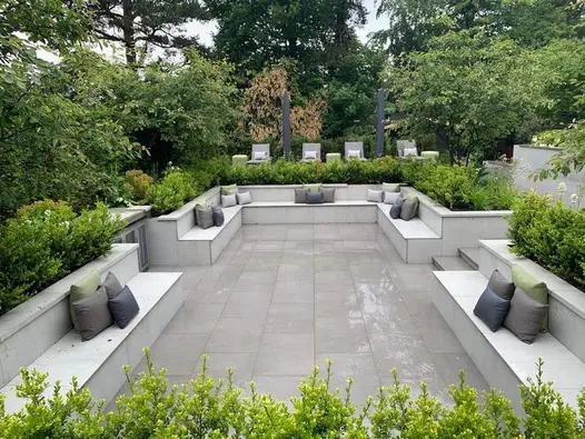 Sunken patio paved with Steel Grey porcelain, benches built in around all sides and raised planted flower beds.