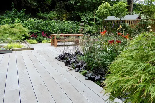 Table and benches sit on Smoked Oak Millboard Decking with planted borders in fenced garden. Built by Simply Green Landscapes.