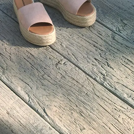 Close-up of Driftwood Millboard decking, showing realistic grain and antique look of planks. 2 espadrilles at top of picture.