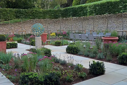 Tall dry stone retaining walls on either side of garden paved with Harvest sawn sandstone paving inset with formal bed layout.
