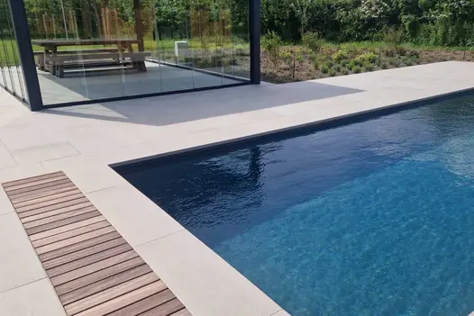 Wooden picnic bench sits under glass pergola on Urban Grey Porcelain patio next to large swimming pool using 40mm Downstand steps.