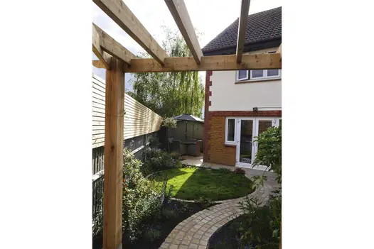 view of a curvy path made from Mint Sandstone Setts runs through a wooden pergola, flanked by planting beds on either side.