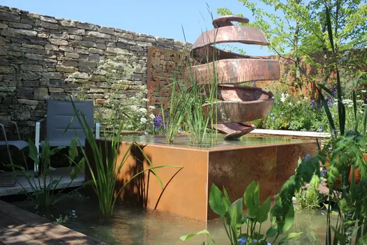 Pond has a raised water feature in with steel corten designclad and other steel corten elements, surrounded by rustic brick wall.