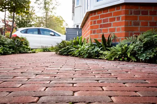 White car on far side of front garden laid with Winton clay pavers between lushly planted beds. Built by Nordland landscapes.