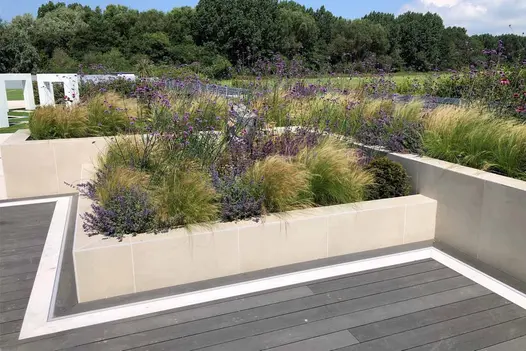 Softly planted raised beds faced with Off White exterior cladding sit next to composite decking, with modern henge in background.