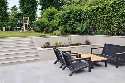 Bullnose Steps rise to lawn with swings and slides from porcelain-paved patio with Off White exterior cladding on retaining walls.