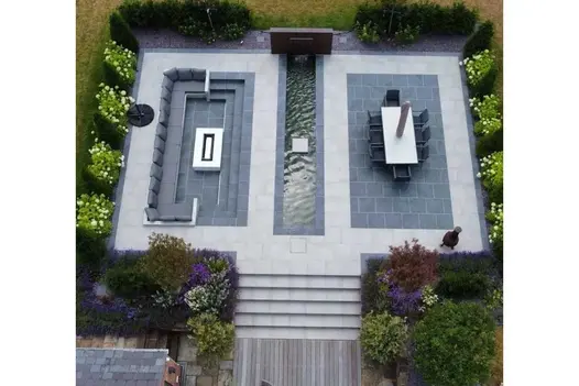 View from above of steps up to seating and dining areas either side of long pond, laid with Slab Coke and Cement outdoor tiles.