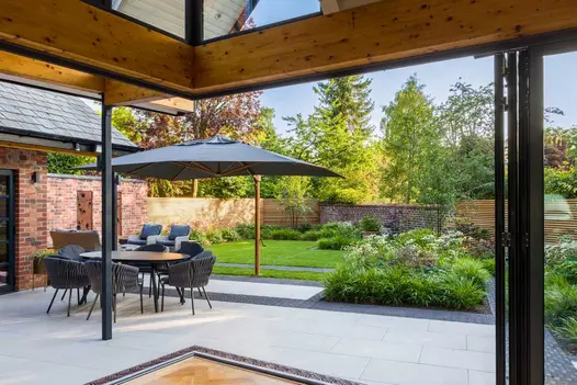 Patio of Florence Grey porcelain paving and clay pavers with table and chairs under cantilevered parasol. Lawn beyond.