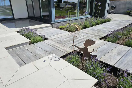 Butterfly shadow dances on florence grey porcelain paving with statue of pixie chasing with a net. Cinder porcelain also used.