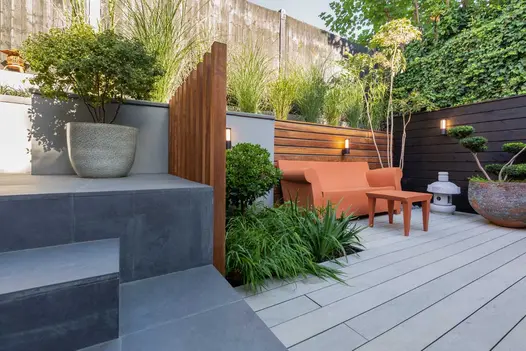 Slab Coke porcelain steps and risers down to courtyard with grey decking and tan-colour furniture. Built by Olive Tree Landscaping.