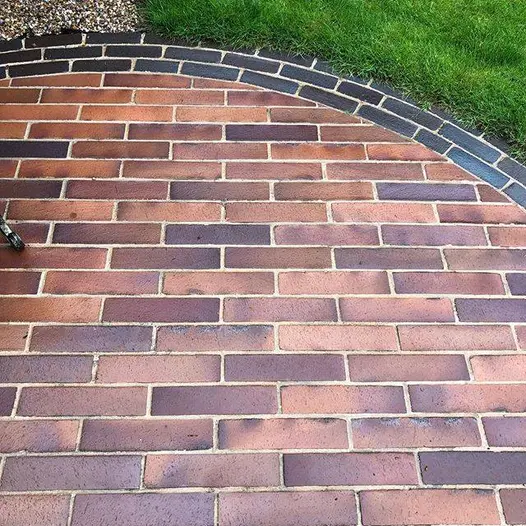Curved edge of wet Lugano brick paving, set into lawn, provides border to Bromley clay pavers laid in running bone pattern.