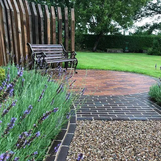 Curved edge of Lugano brick paving encircles Bromley Clay pavers, set between lawn and flower bed. Built by Outsiders Landscaping.