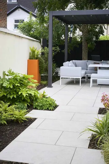 half-view of grey pergola with furniture underneath, astor grey porcelain paving leads up with planting either side.