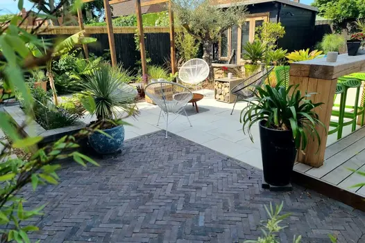 Wooden bar, studio, various shaped pots and exotic planting in busy garden paved with slabs and Lugano Dutch clay pavers.