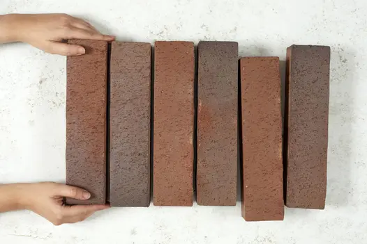 Against plain white background, 2 hands add a 6th Bromley clay paver to a row of 5, with the 4th slightly displaced.