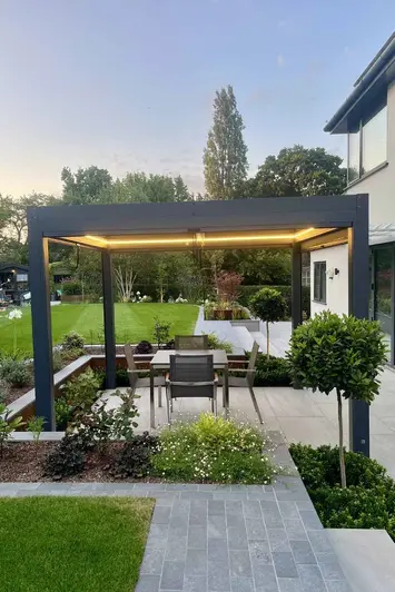 Dusk view shows proteus pergola with led lights above porcelain patio with platinum grey porcelain setts as path leading towards.