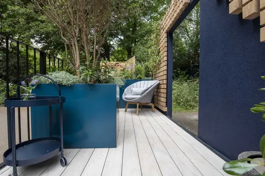 Large planters on Polar DesignBoard composite decking, between railings and blue wall in The Reading Room garden, RHS Chelsea 2023.