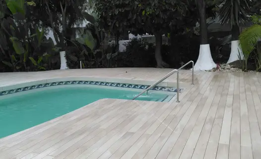 Steps lead down into curved swimming pool surrounded by polar designboard composite decking and huge leafy trees and plants 