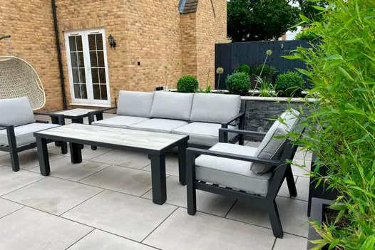 A grey metal garden lounging set in a rear suburban garden set on top of a Polished Concrete porcelain patio.