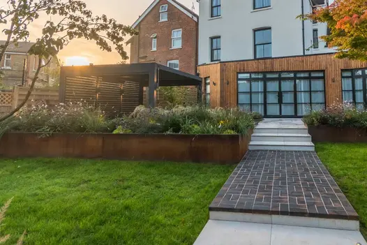 Long raised bed, faced with Steel Corten external cladding, creates border between lawn and patio. Design by Kitti Kovacs.