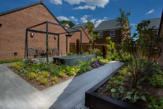 Large raised and low level flower beds with Cinder porcelain pathways cutting through and a large block water feature.
