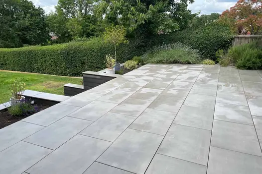 Side view of polished concrete porcelain paving shown in wet conditions, hedges line the garden with steps down to lawn.