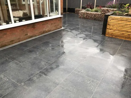 Charcoal porcelain paved patio outside a conservatory surrounded on one side by raised beds made from timber and gabion cages.