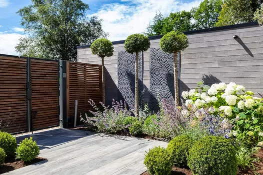 Colourful garden courtyard with vibrant flower beds and a porcelain patio set against a timber clad building.