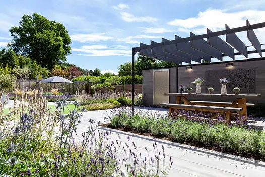 Large country garden with porcelain patio and seating area underneath a bespoke pergola type structure.
