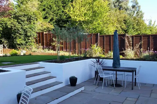 Sunken patio using raj green indian sandstone paving has steps leading up to lawn area with flowerbeds surrounding.