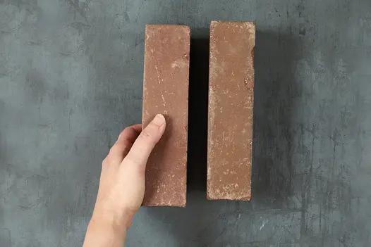 Hand places a Roma Clay Paver into formation of 1 other brick arranged on dark background. Free UK delivery available.